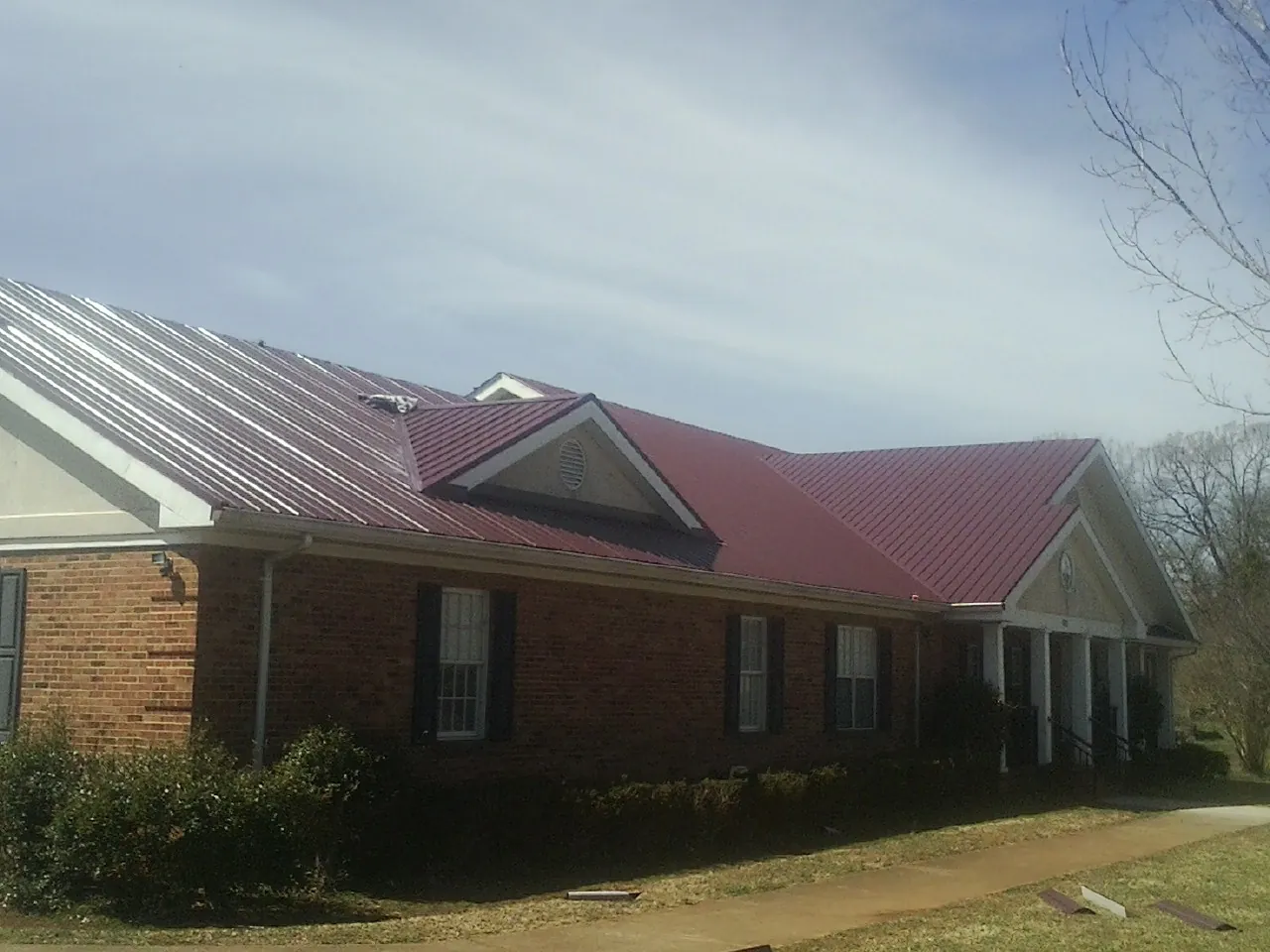 Red metal roof with gabled entries on a long brick building, from a Hail Damage Roof Repair job in Burnettsville