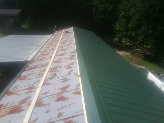 Old rusted panels beside newly installed green metal roofing — Wind Damage Roof Repair by Roofing Brothers in Burnettsville