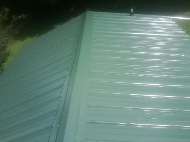 New green metal panels meeting at the ridge of a roof — Flat Roof Repair work by our crew in Burnettsville