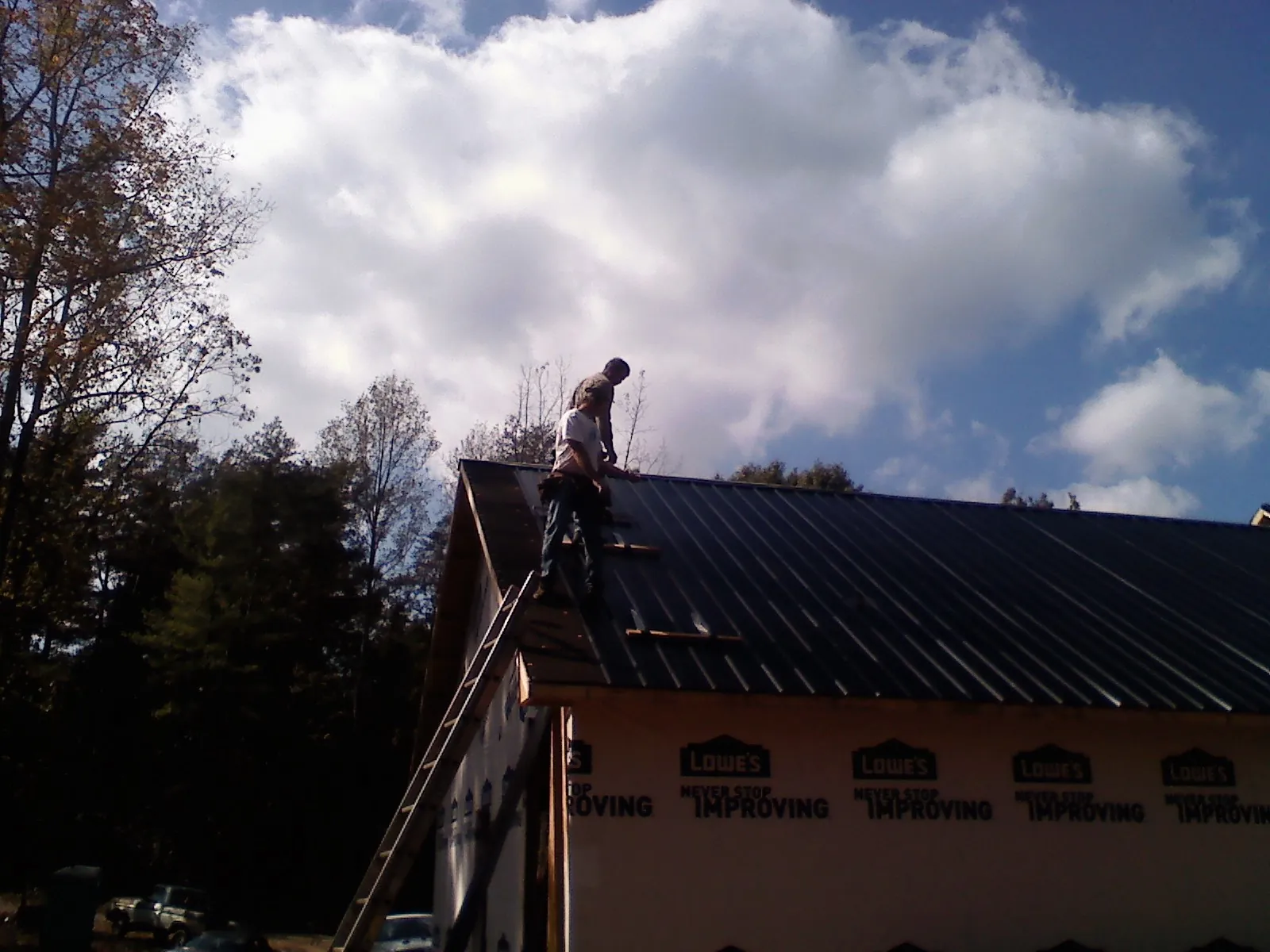 Roofer fastening dark metal panels high against a cloudy sky, from a Roof Inspection job in Burnettsville
