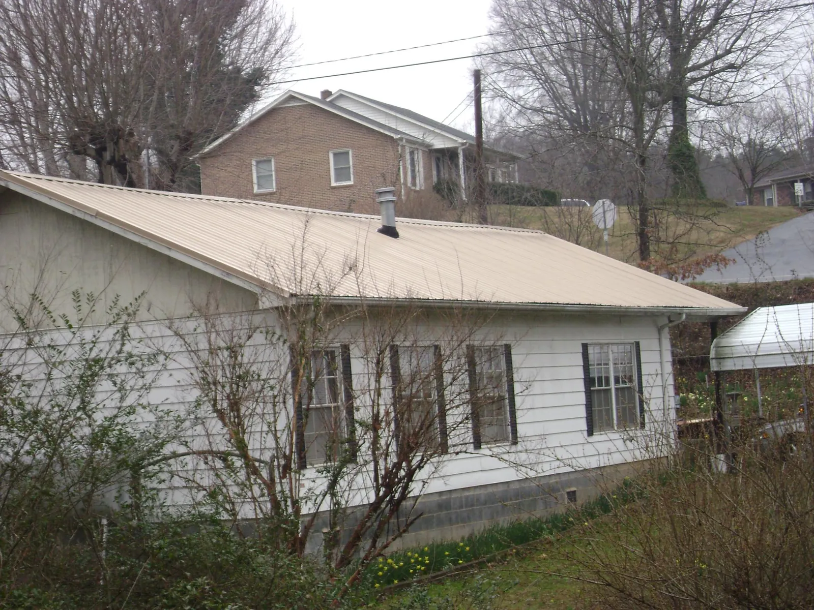 Tan metal roof on a white sided house set into a hillside — Commercial Roofing by Roofing Brothers in Burnettsville