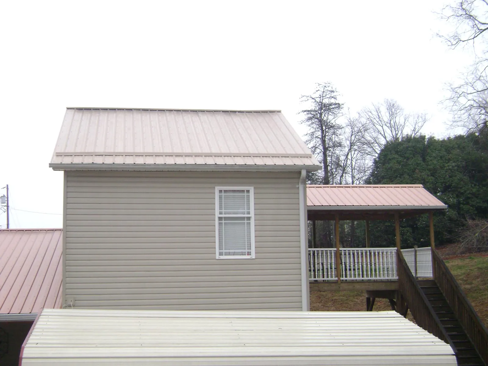 Tan metal roofs on a two story addition and attached porch, from a Roof Replacement job in Burnettsville